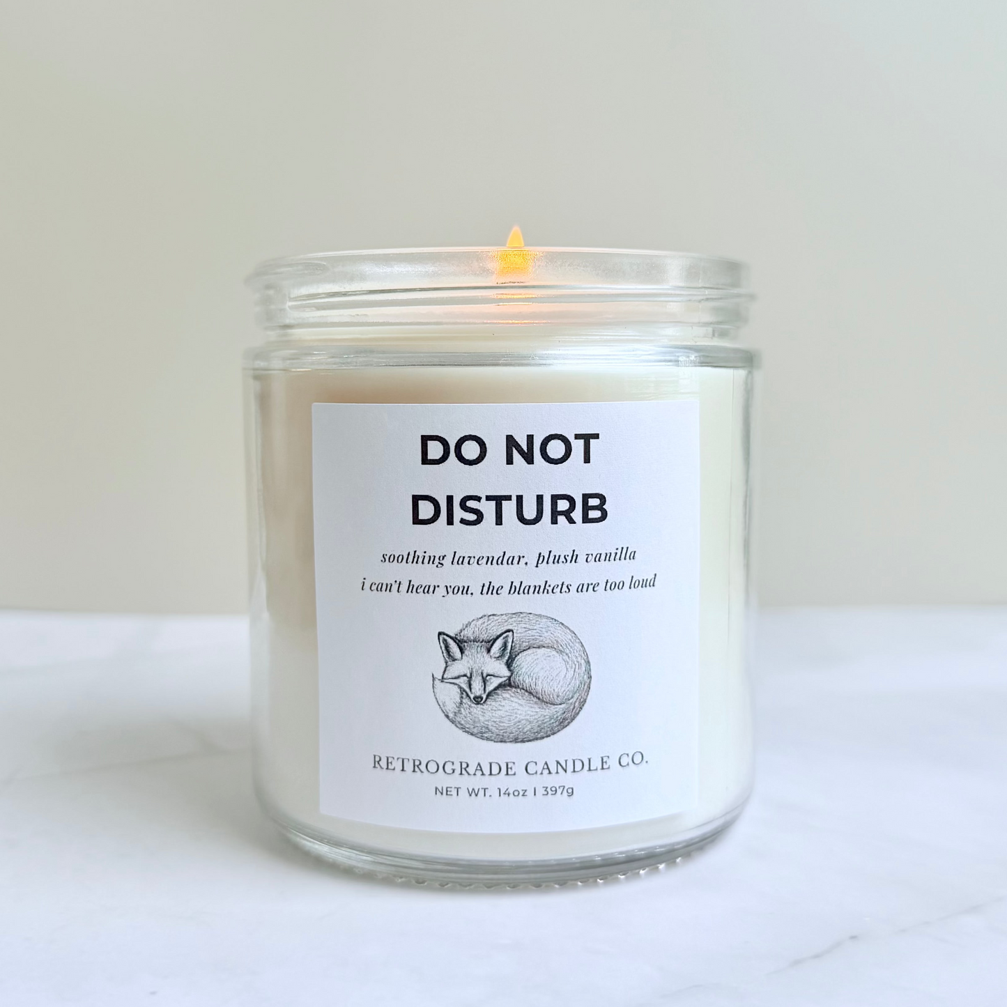 Candle in a glass jar with a label on a white surface with sleeping fox graphic illustration and do not disturb title