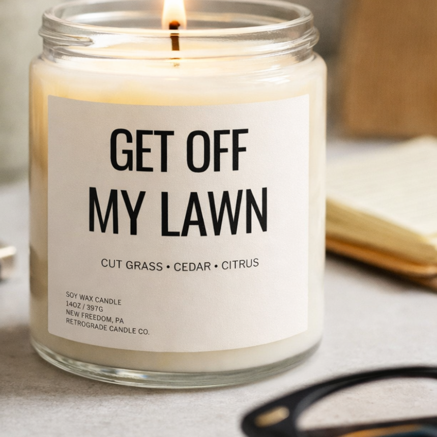Candle in a glass jar with a label reading 'Get Off My Lawn' on a table.