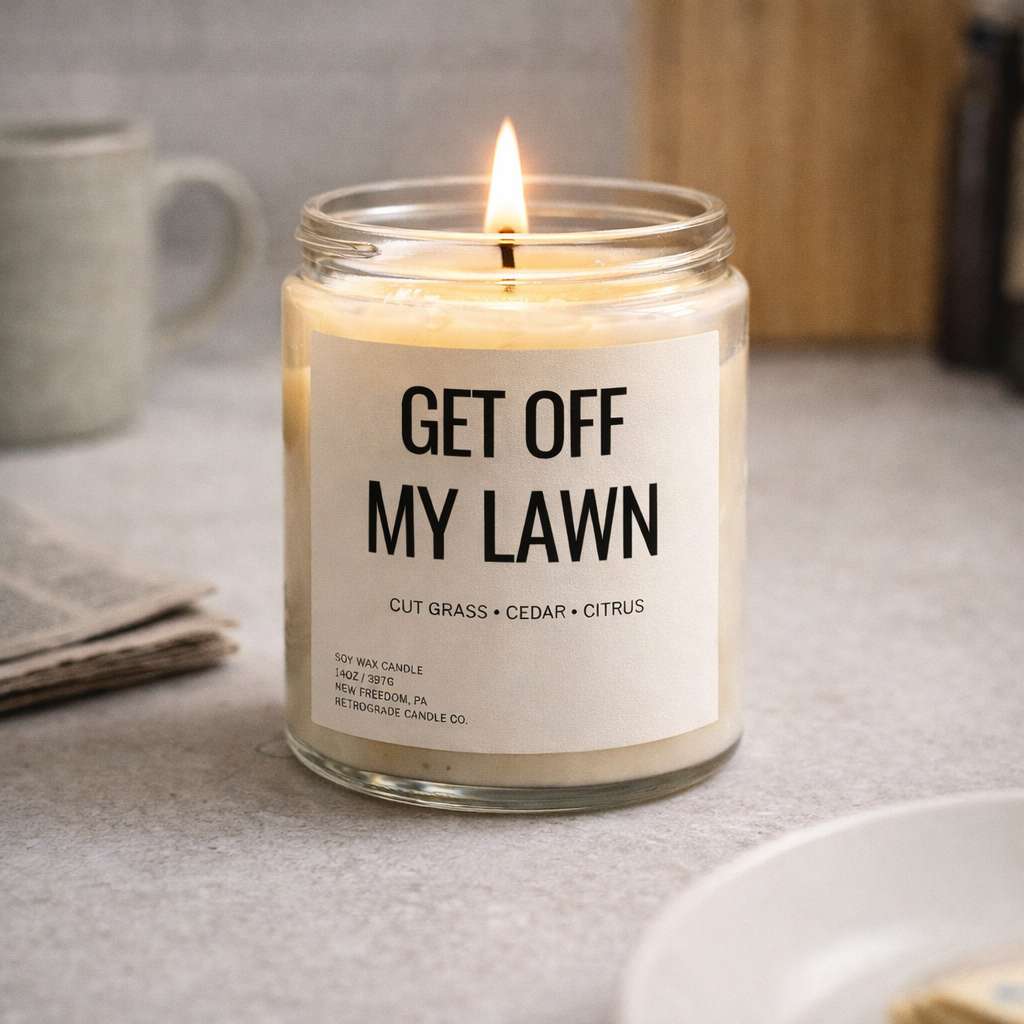 Candle in a glass jar with a label reading 'Get Off My Lawn' on a table.