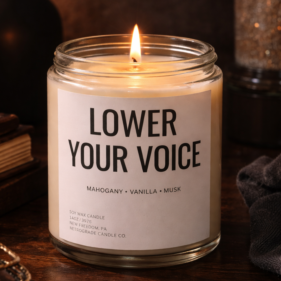 Candle in a glass jar with a label reading 'Lower Your Voice' on a wooden surface.