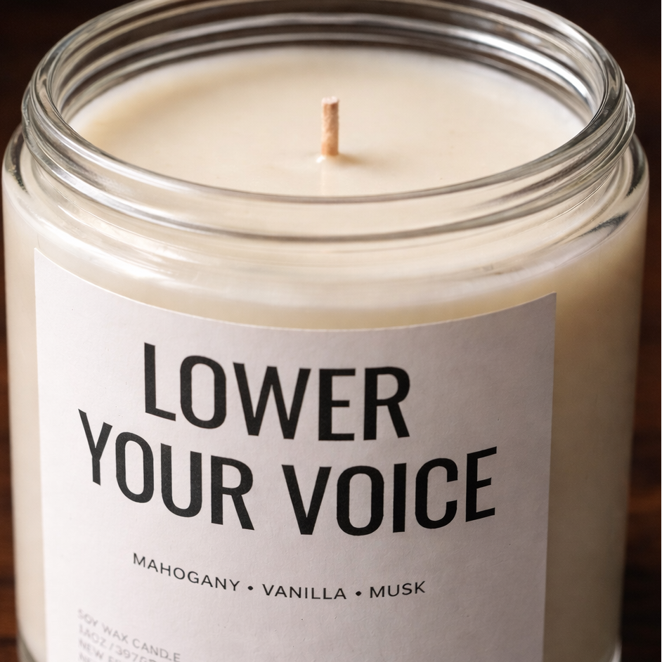 Candle in a glass jar with a label reading 'Lower Your Voice' on a wooden surface.