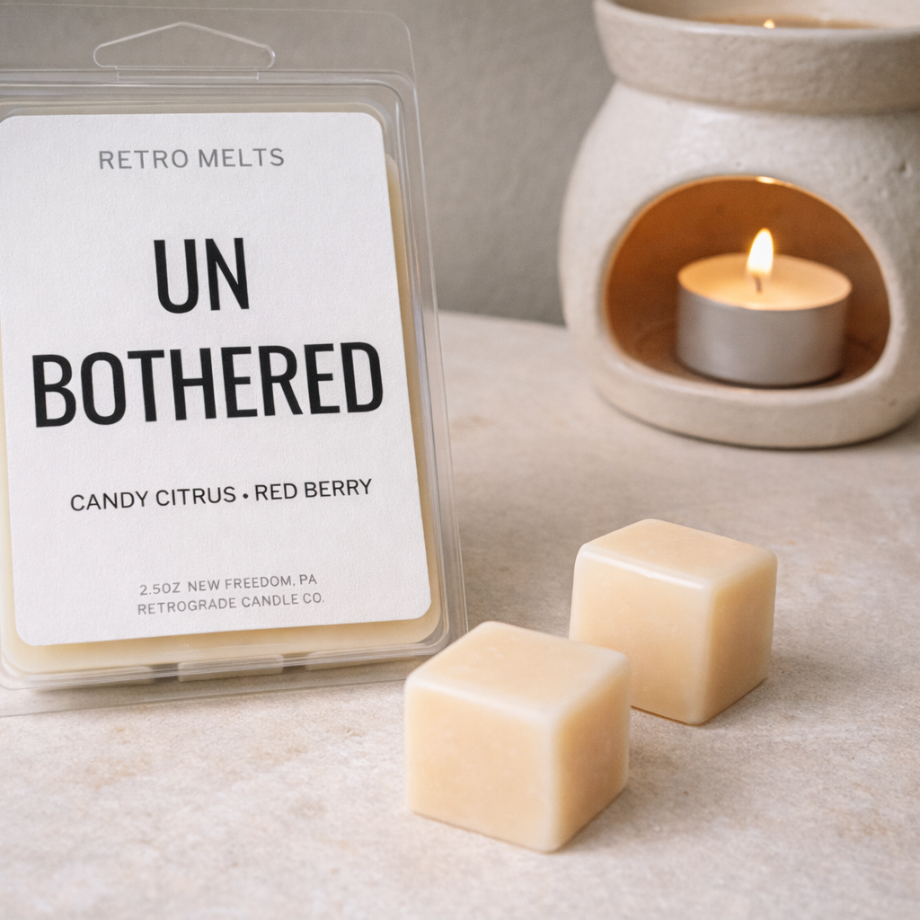 Packaged candle melts labeled 'Un Bothered' with two melts on a surface next to a lit candle.